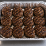 Half-size aluminum catering tray filled with 12 grilled Cajun meatballs, cooked over an open flame and arranged neatly for catering service.