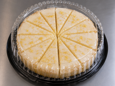 Whole limoncello cake pre-sliced into 12 wedges and displayed in a round black plastic container with a clear dome lid.