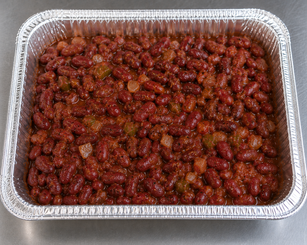 Half-size aluminum catering tray filled with slow-cooked Cajun red beans in a rich seasoned sauce, prepared for catering service.