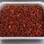 Half-size aluminum catering tray filled with slow-cooked Cajun red beans in a rich seasoned sauce, prepared for catering service.