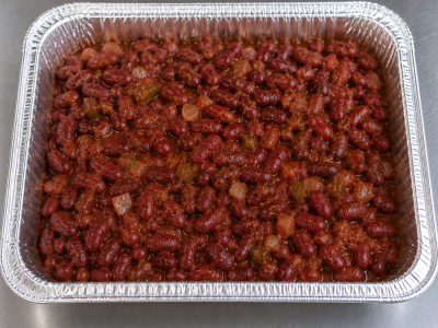 Half-size aluminum catering tray filled with slow-cooked Cajun red beans in a rich seasoned sauce, prepared for catering service.